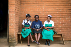 Two m2m Nurses sat on a bench with an m2m Mentor Mother, smiling at the camera.